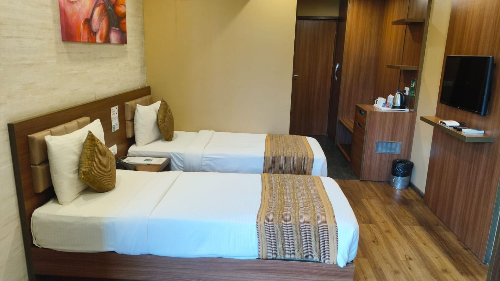 A side view of the room with twin beds, highlighting the room amenities such as an LED TV, wall frame, and a passage leading to the entrance door at Le ROI Digha Hotel, West Bengal.